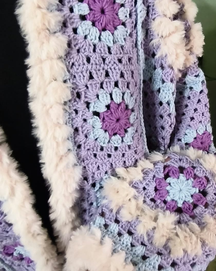 Dettaglio di un cardigan all'uncinetto lilla con bordo effetto pelliccia